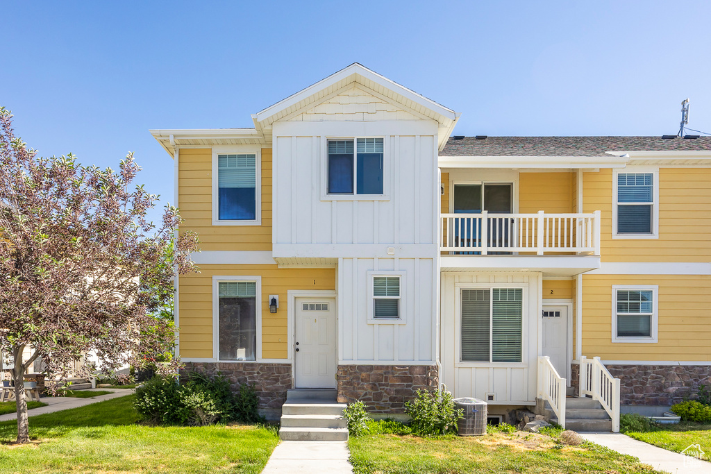 View of front of house with central air condition unit, a balcony, and a front lawn