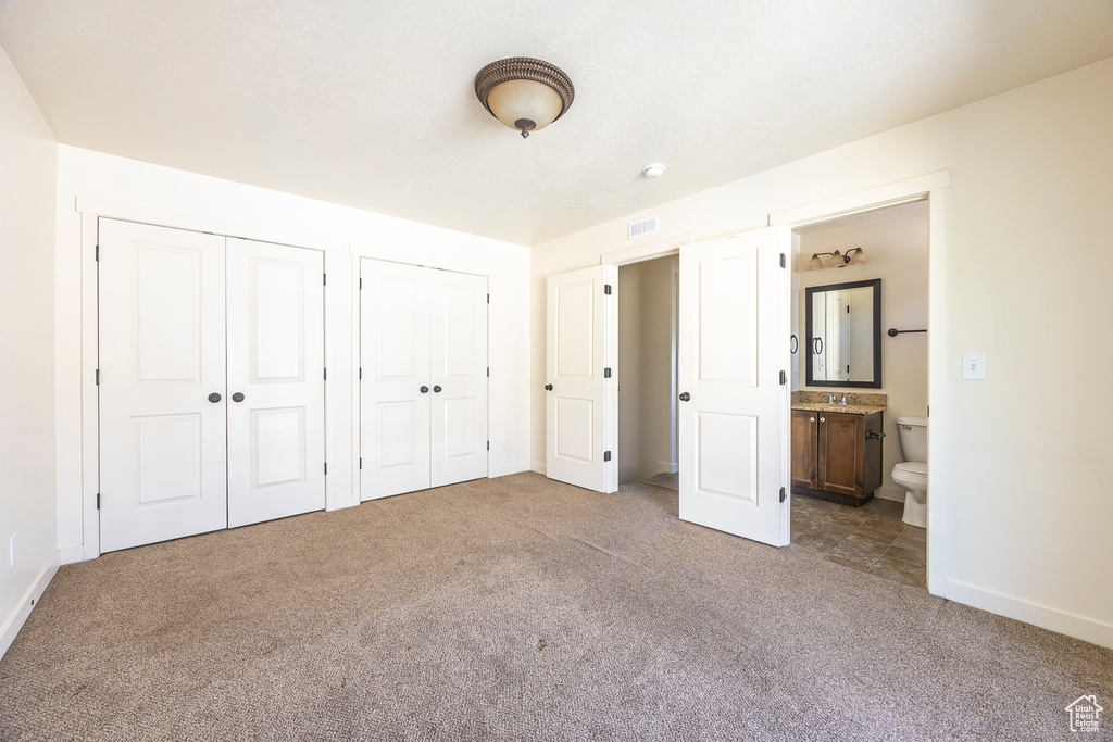 Unfurnished bedroom featuring sink, dark colored carpet, connected bathroom, and multiple closets