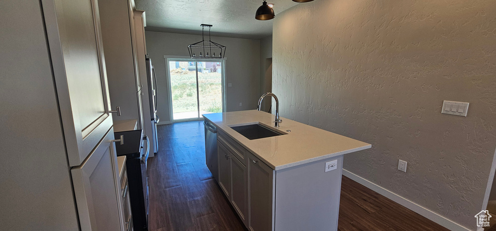 Kitchen featuring a center island with sink, sink, decorative light fixtures, stainless steel dishwasher, and dark hardwood / wood-style floors