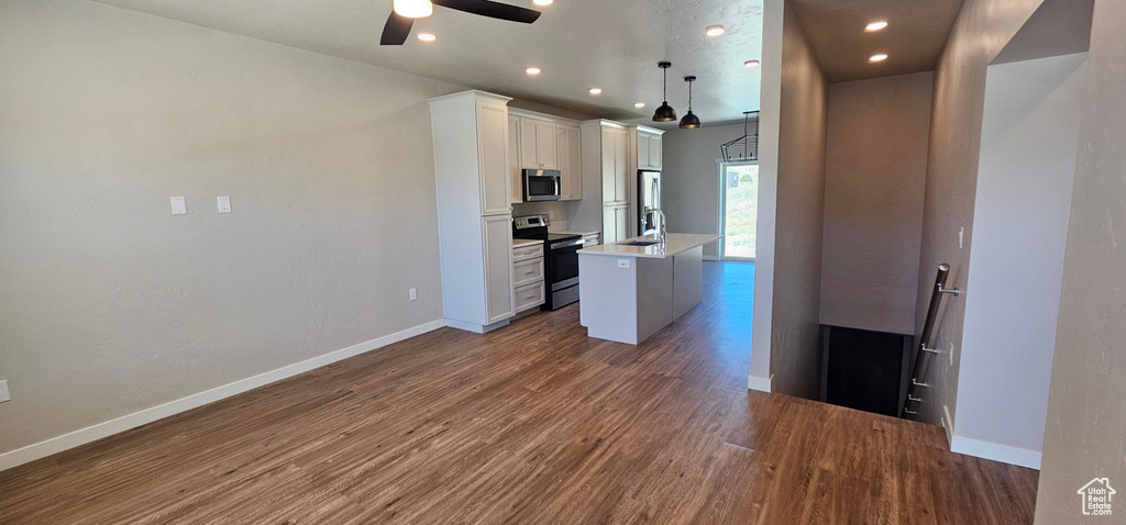 Kitchen with white cabinets, dark hardwood / wood-style flooring, appliances with stainless steel finishes, and an island with sink