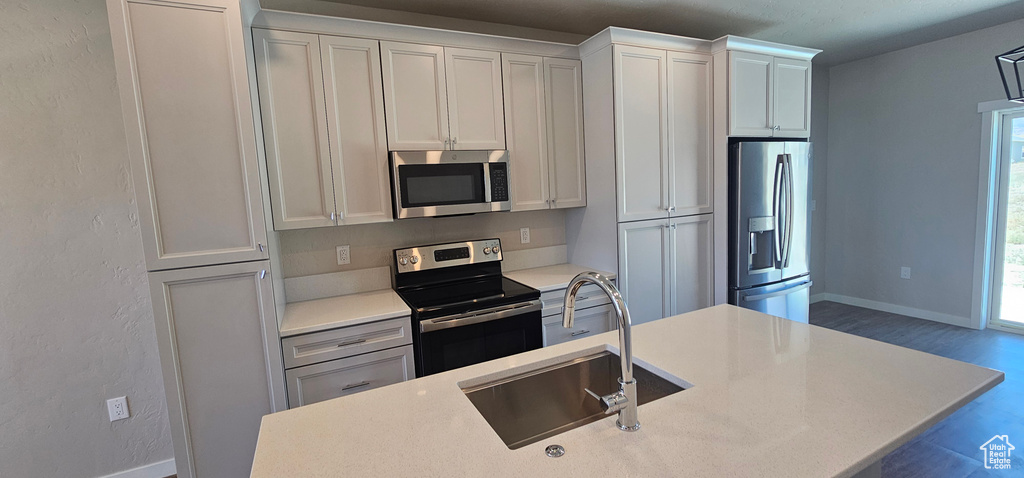 Kitchen with sink, appliances with stainless steel finishes, white cabinets, and hardwood / wood-style floors