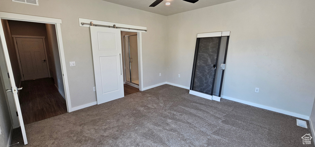 Unfurnished bedroom featuring a barn door, ceiling fan, and dark carpet