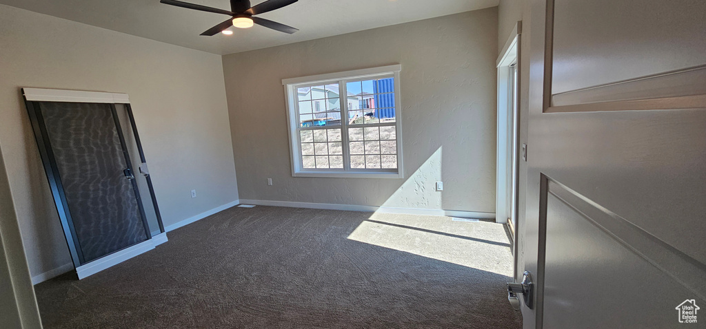 Unfurnished bedroom with dark carpet and ceiling fan