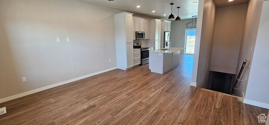 Kitchen featuring stainless steel appliances, pendant lighting, white cabinets, a center island with sink, and dark hardwood / wood-style floors