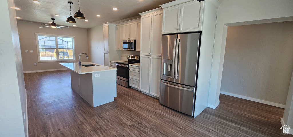 Kitchen with appliances with stainless steel finishes, sink, a kitchen island with sink, white cabinetry, and dark hardwood / wood-style flooring