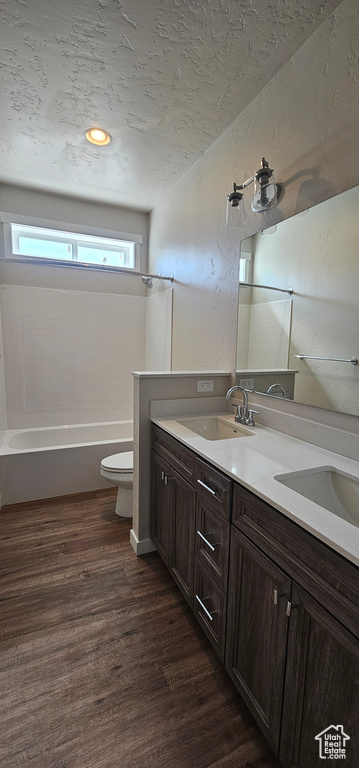 Full bathroom featuring hardwood / wood-style floors, tub / shower combination, a textured ceiling, toilet, and dual bowl vanity