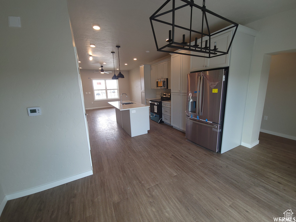 Kitchen with white cabinetry, dark wood-type flooring, stainless steel appliances, a kitchen island with sink, and decorative light fixtures