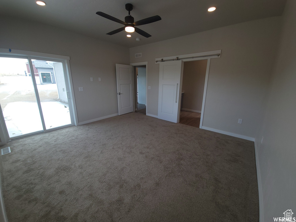 Unfurnished bedroom with carpet flooring, a barn door, ceiling fan, and access to exterior