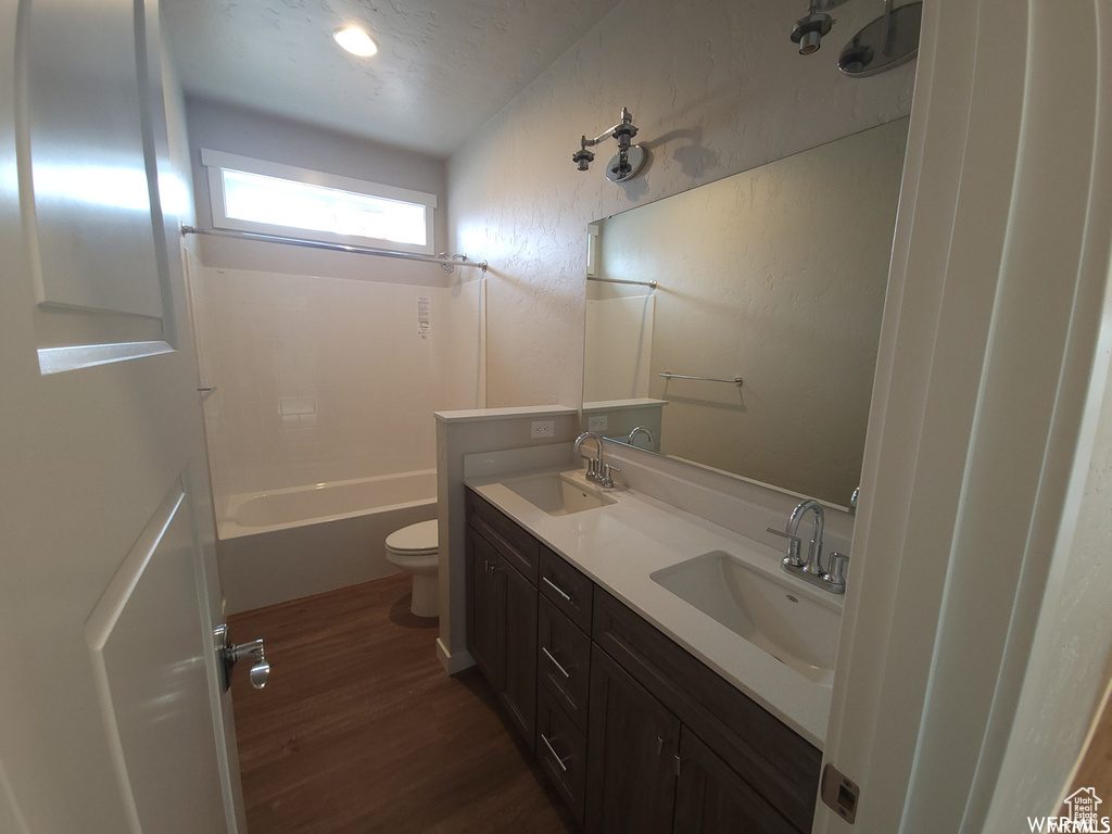 Full bathroom with dual sinks, hardwood / wood-style floors, washtub / shower combination, toilet, and large vanity