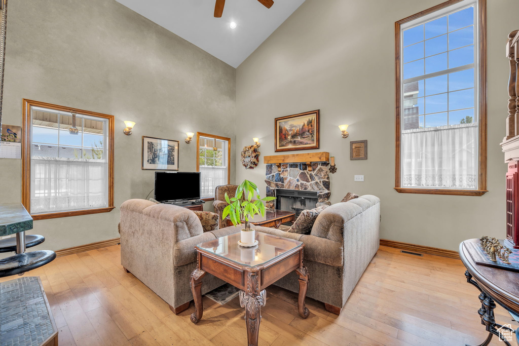 Living room with high vaulted ceiling, ceiling fan, a stone fireplace, and light hardwood / wood-style flooring