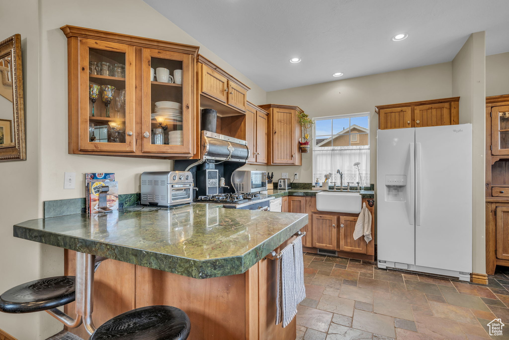 Kitchen featuring kitchen peninsula, white refrigerator with ice dispenser, ventilation hood, tile floors, and sink