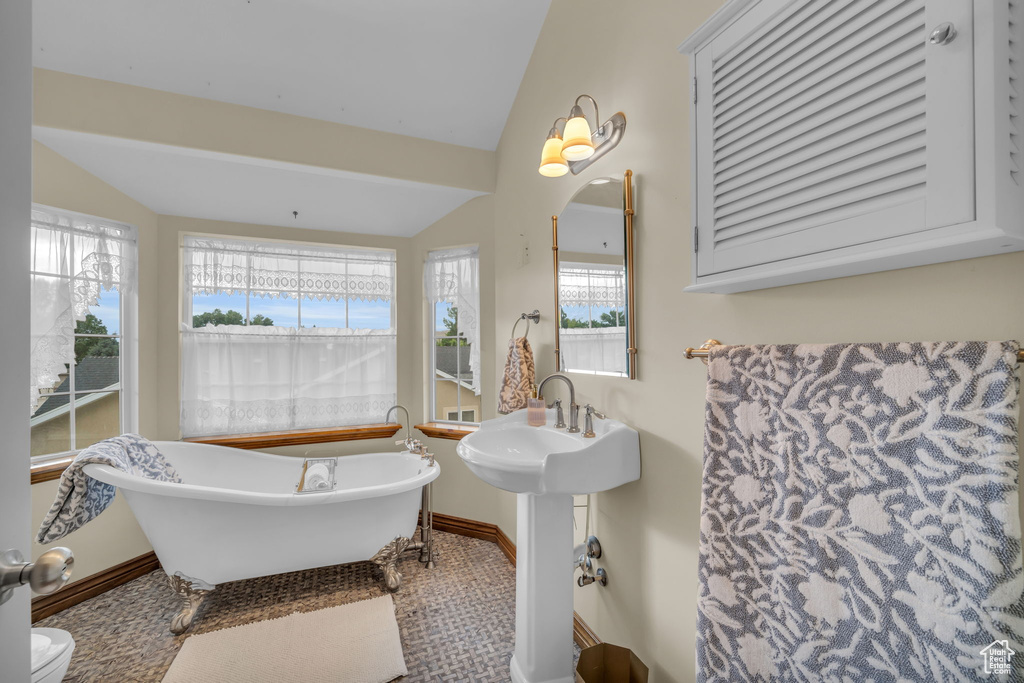 Bathroom with a wealth of natural light, vaulted ceiling, toilet, and a bathing tub