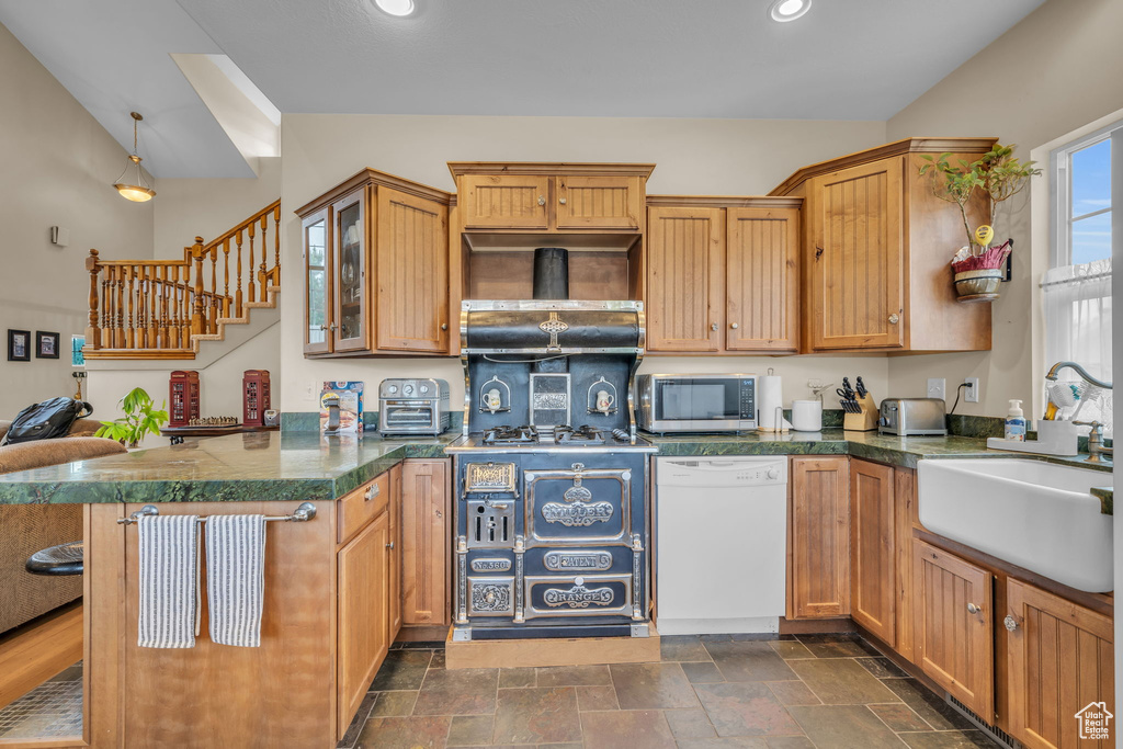 Kitchen with kitchen peninsula, a kitchen bar, dark tile flooring, white dishwasher, and sink