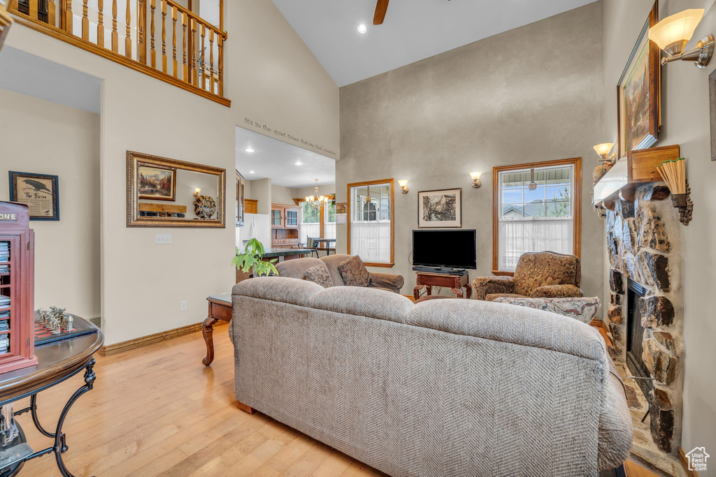 Living room featuring high vaulted ceiling, ceiling fan with notable chandelier, light wood-type flooring, and a stone fireplace