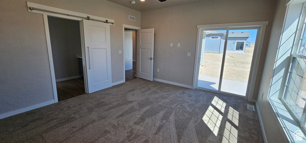 Unfurnished bedroom featuring a barn door, multiple windows, dark carpet, and access to exterior