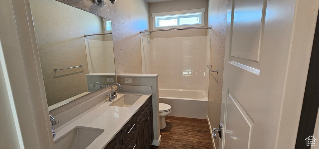 Full bathroom with dual bowl vanity, shower / washtub combination, hardwood / wood-style flooring, and toilet