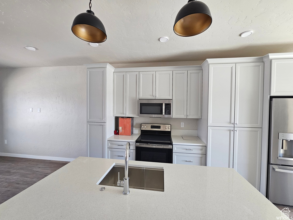 Kitchen featuring pendant lighting, dark wood-type flooring, sink, white cabinetry, and appliances with stainless steel finishes