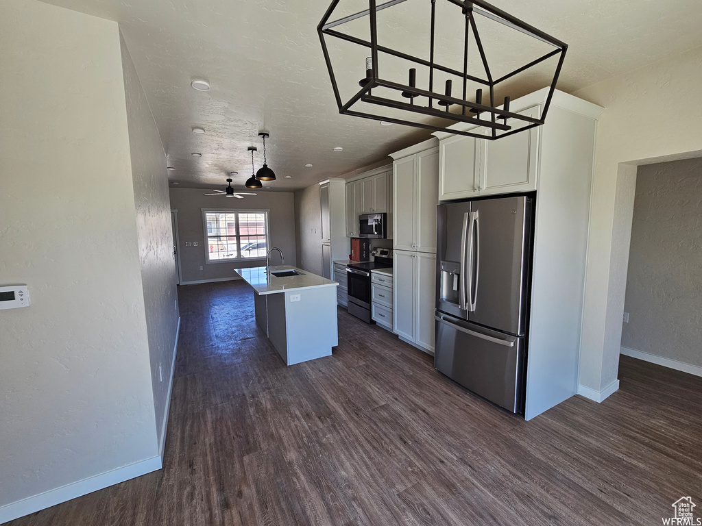 Kitchen featuring white cabinets, hanging light fixtures, an island with sink, dark wood-type flooring, and appliances with stainless steel finishes