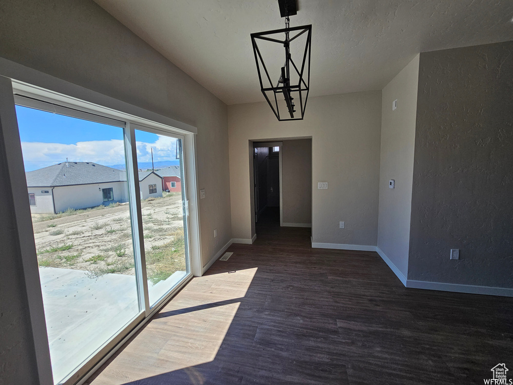 Unfurnished dining area featuring a notable chandelier, plenty of natural light, and dark hardwood / wood-style flooring