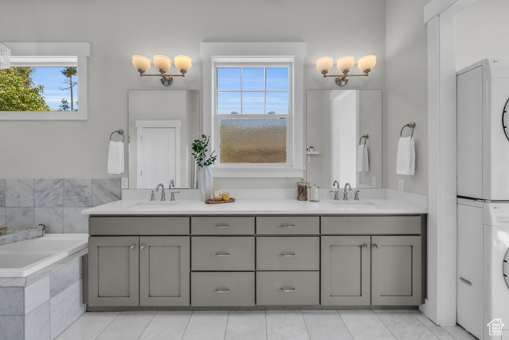 Bathroom with a healthy amount of sunlight, dual vanity, and stacked washer / drying machine