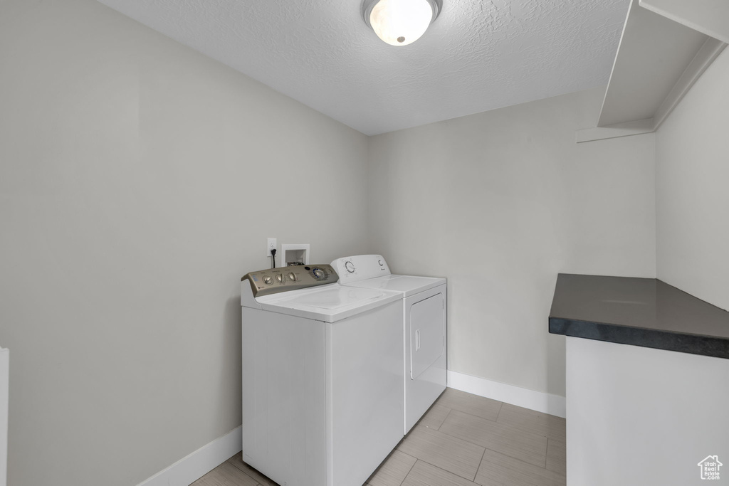 Laundry area with hookup for a washing machine, a textured ceiling, independent washer and dryer, and light tile floors