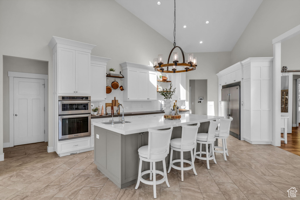 Kitchen featuring stainless steel appliances, a center island with sink, high vaulted ceiling, sink, and white cabinets