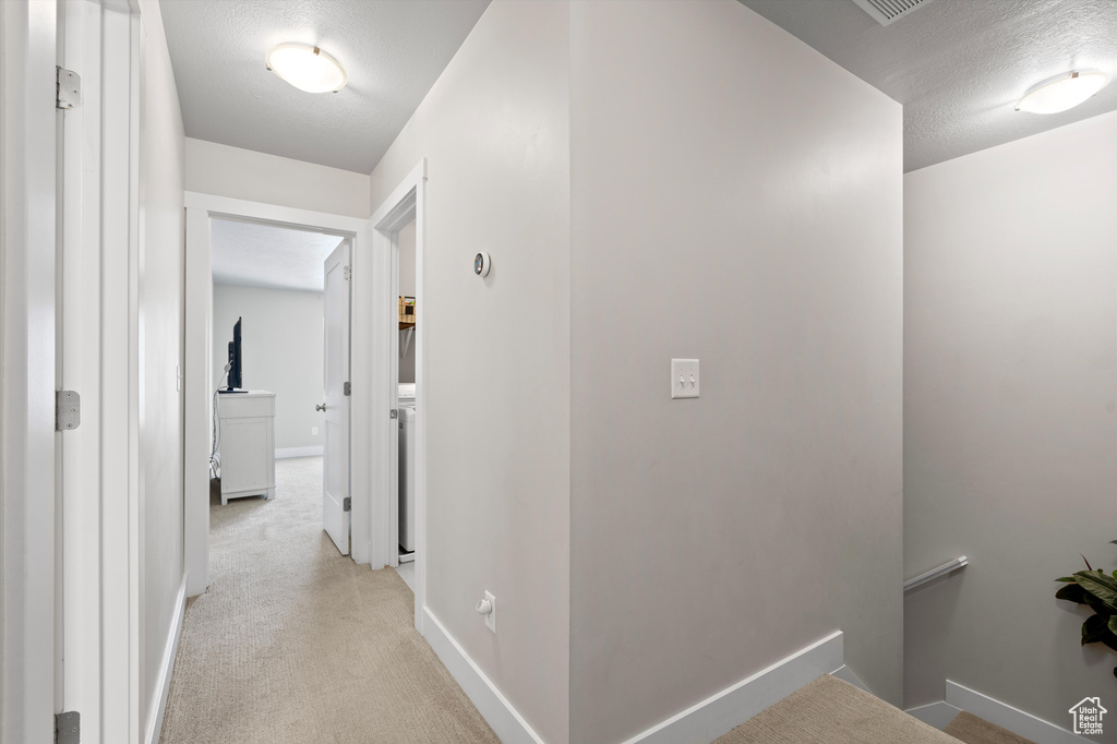 Hallway featuring a textured ceiling and light carpet