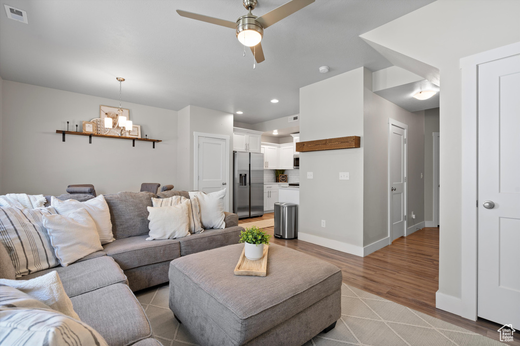 Living room featuring ceiling fan with notable chandelier and light hardwood / wood-style floors