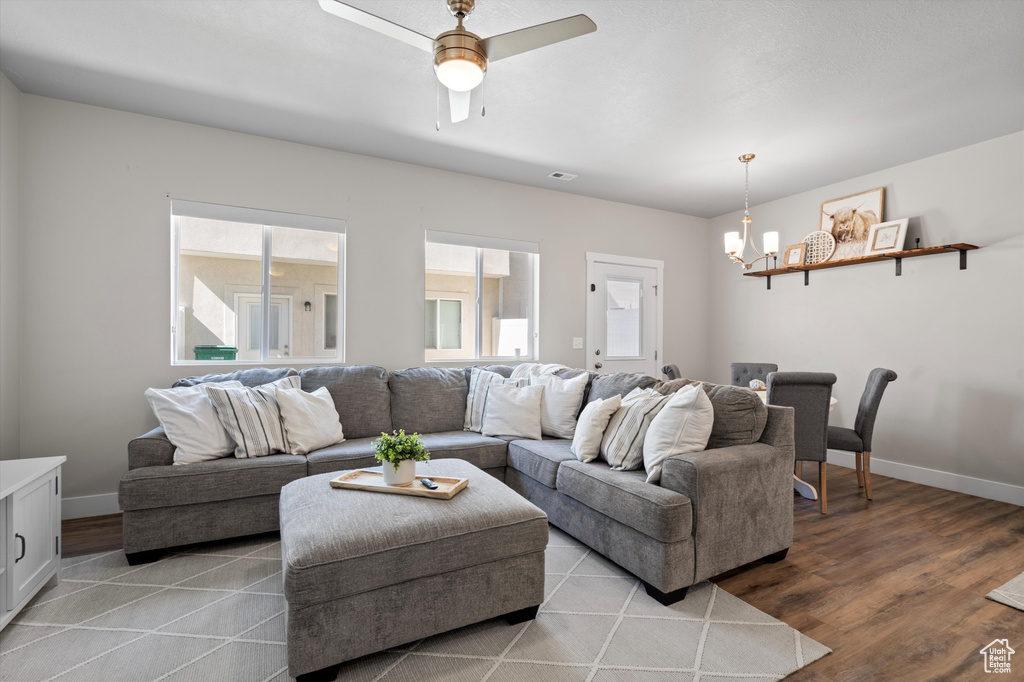 Living room with ceiling fan with notable chandelier and wood-type flooring