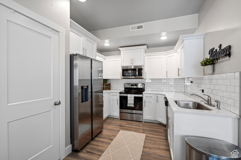 Kitchen with stainless steel appliances, tasteful backsplash, white cabinetry, dark wood-type flooring, and sink