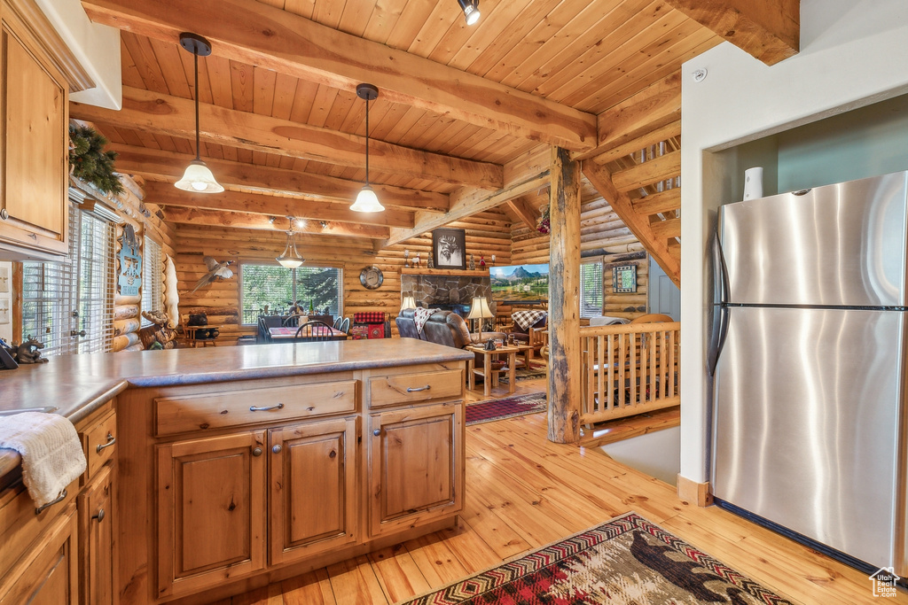 Kitchen with light hardwood / wood-style flooring, log walls, pendant lighting, and stainless steel fridge