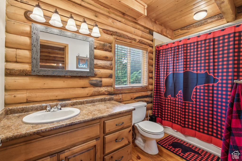 Bathroom featuring rustic walls, wood ceiling, vanity, and toilet