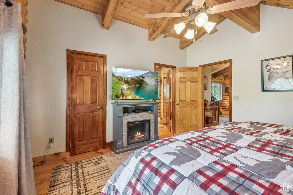 Bedroom featuring vaulted ceiling with beams, light hardwood / wood-style flooring, a stone fireplace, wood ceiling, and ceiling fan