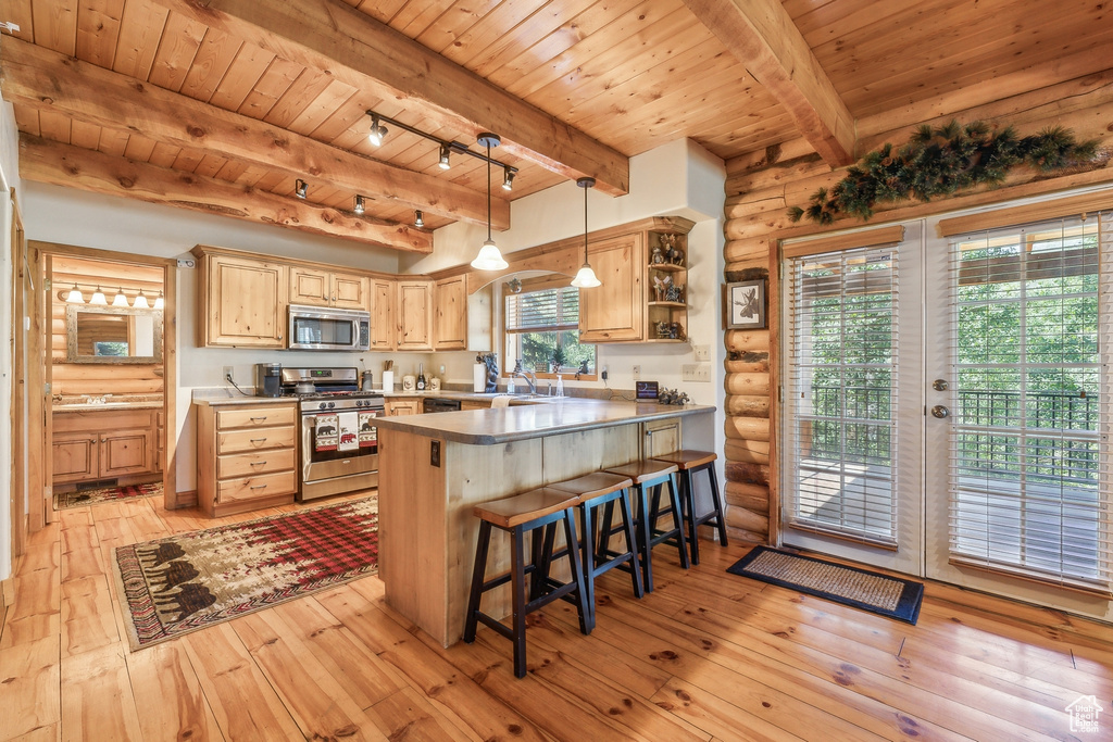 Kitchen with kitchen peninsula, rail lighting, beam ceiling, appliances with stainless steel finishes, and log walls