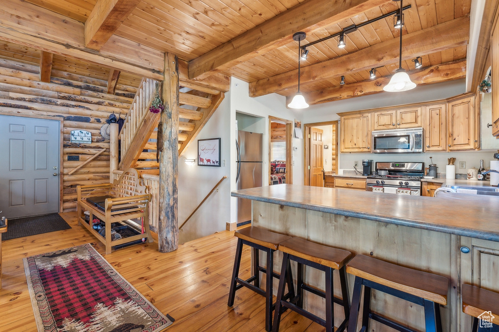 Kitchen with light hardwood / wood-style flooring, appliances with stainless steel finishes, log walls, beam ceiling, and track lighting