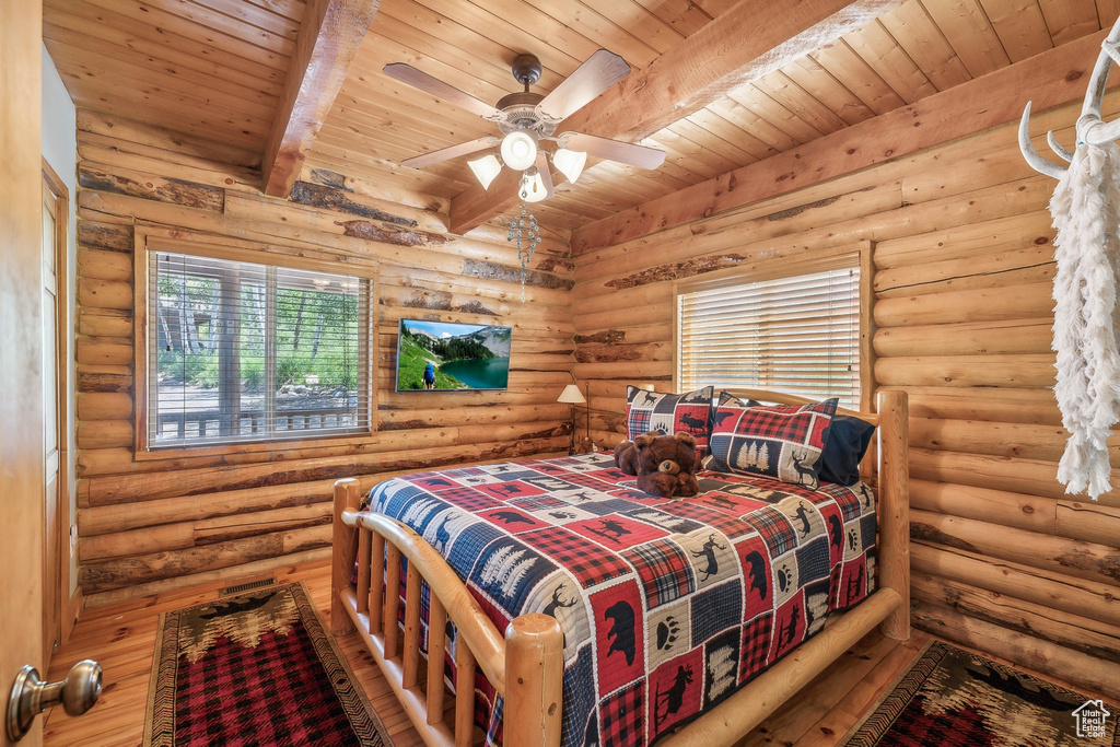 Bedroom featuring beamed ceiling, log walls, hardwood / wood-style floors, wood ceiling, and ceiling fan