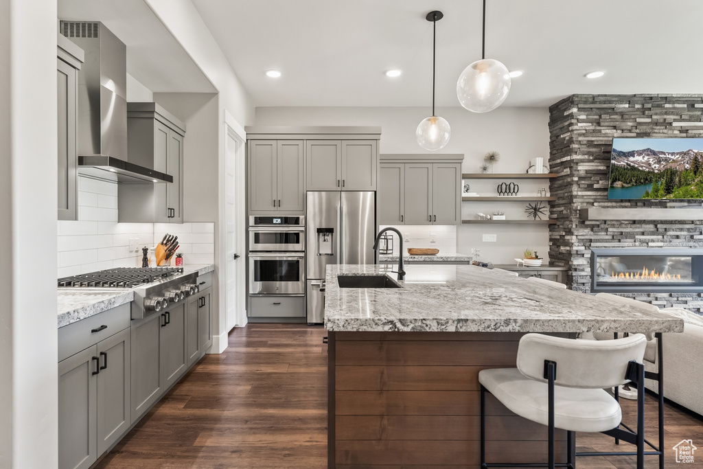 Kitchen with wall chimney range hood, a fireplace, stainless steel appliances, dark hardwood / wood-style floors, and tasteful backsplash