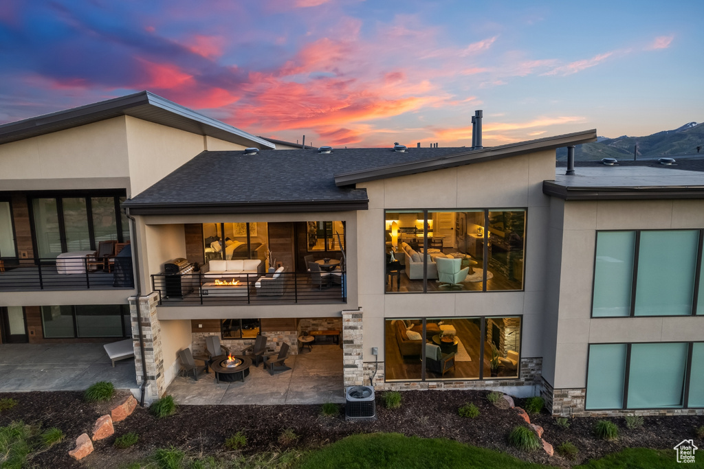 Back house at dusk featuring central AC, a balcony, and a patio