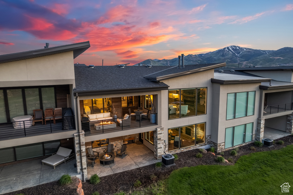 Back house at dusk with central AC, a mountain view, a patio area, and a balcony