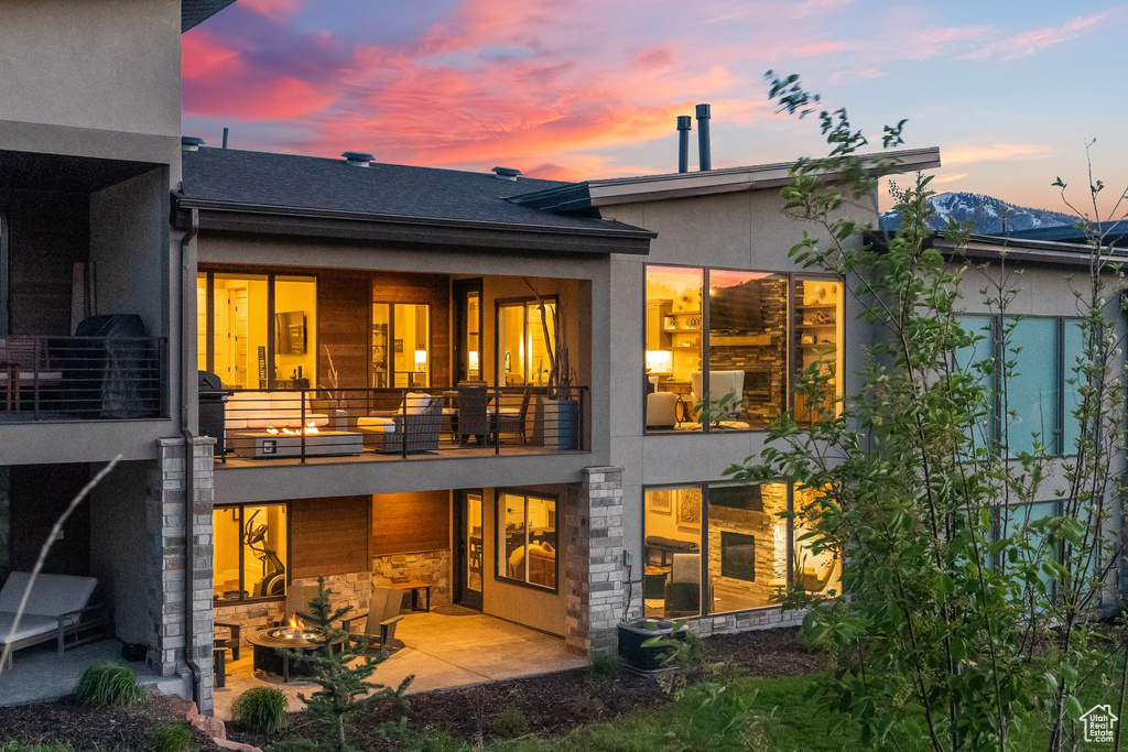 Back house at dusk featuring a patio area and a balcony