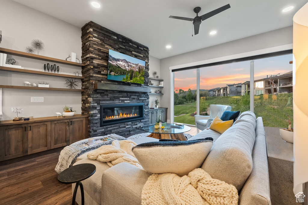 Living room with a stone fireplace, ceiling fan, and dark wood-type flooring