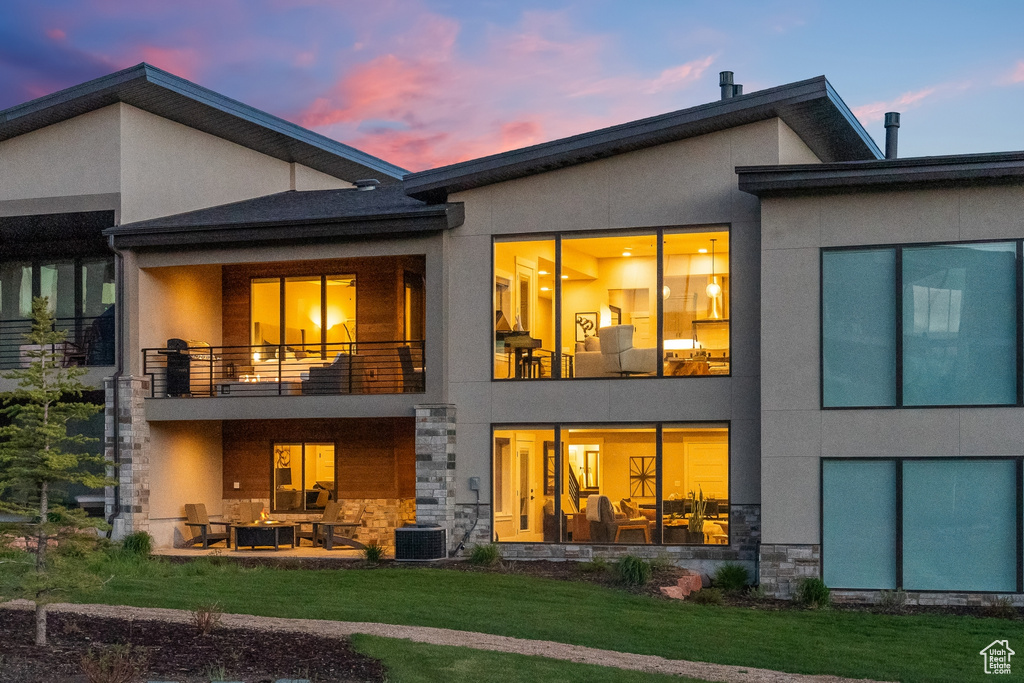 Back house at dusk featuring a patio, central AC, a balcony, and a yard