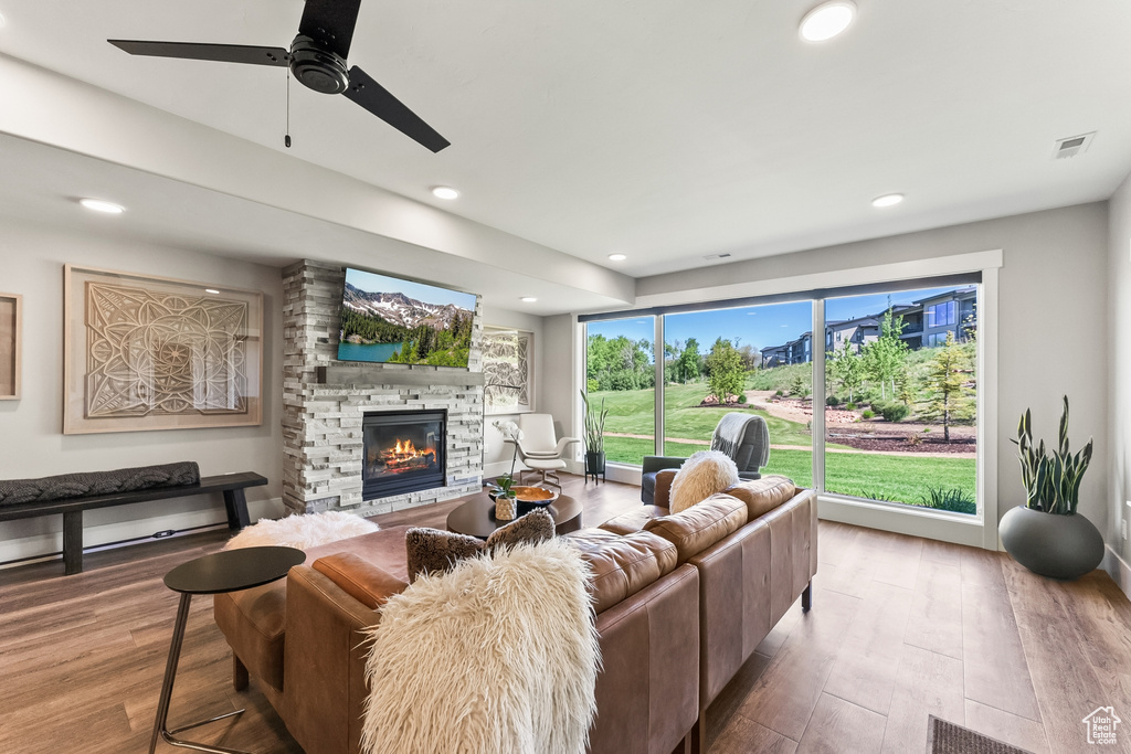 Living room with a stone fireplace, hardwood / wood-style flooring, and ceiling fan