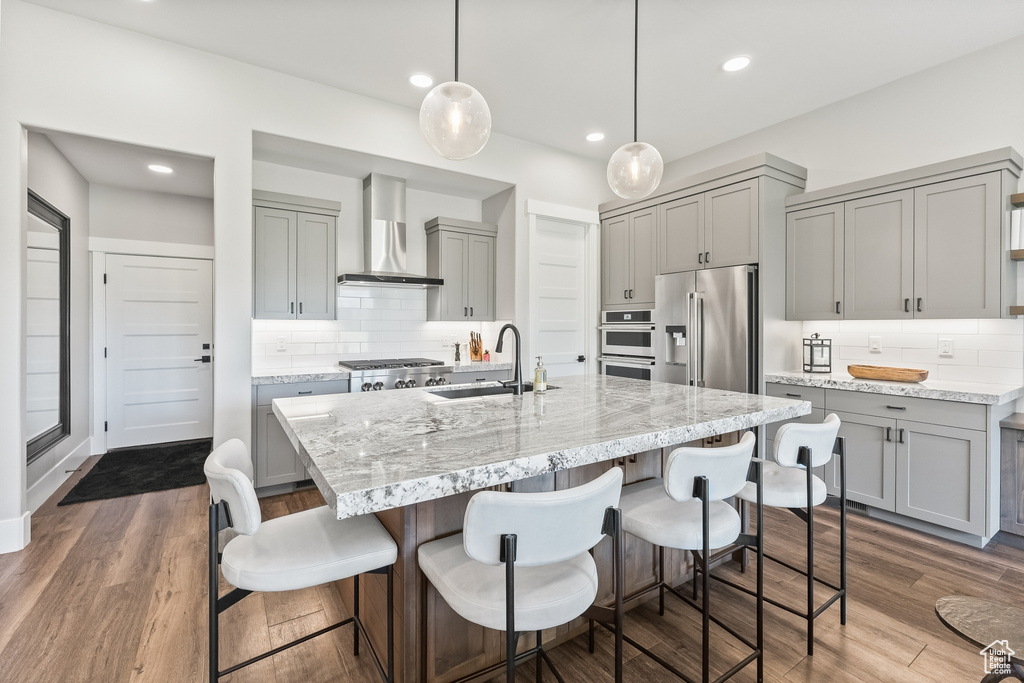 Kitchen featuring hanging light fixtures, wall chimney exhaust hood, stainless steel appliances, and backsplash