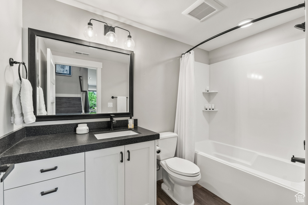 Full bathroom featuring hardwood / wood-style floors, shower / tub combo with curtain, toilet, and vanity