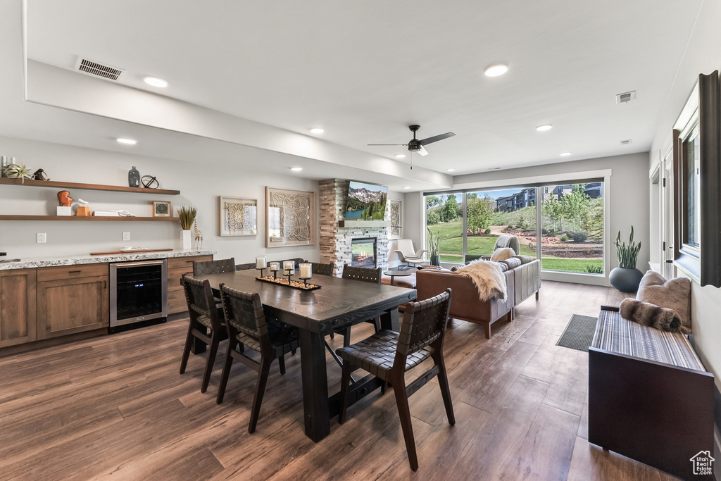 Dining space featuring brick wall, dark hardwood / wood-style flooring, wine cooler, a stone fireplace, and ceiling fan