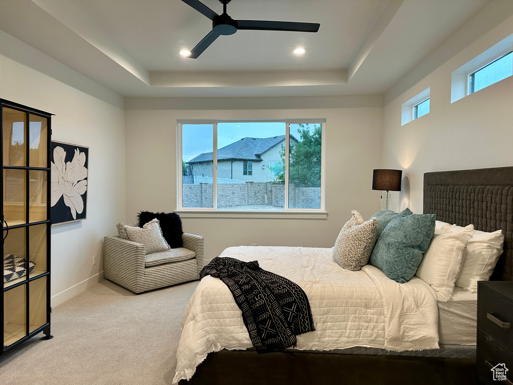 Carpeted bedroom with ceiling fan, a tray ceiling, and multiple windows