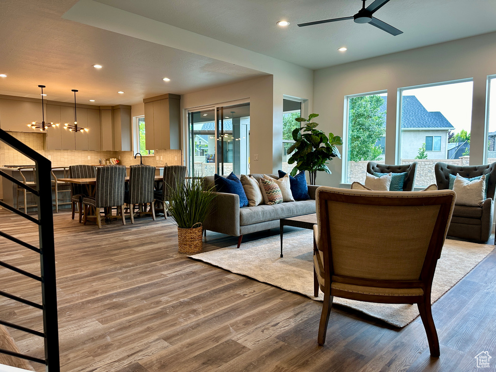 Living room featuring ceiling fan with notable chandelier, sink, and wood-type flooring