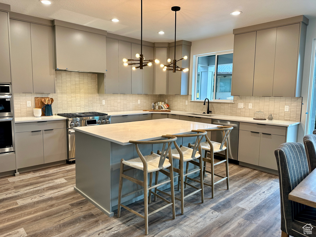 Kitchen with stainless steel appliances, decorative light fixtures, decorative backsplash, hardwood / wood-style floors, and a center island