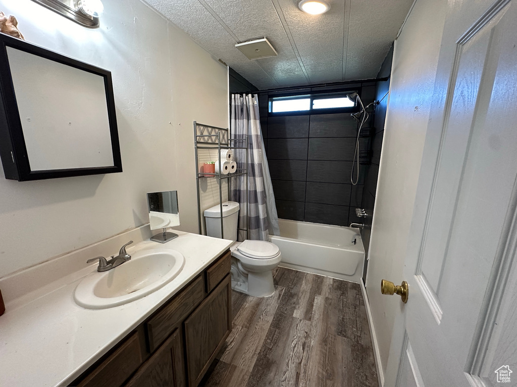 Full bathroom with toilet, wood-type flooring, vanity, a textured ceiling, and shower / tub combo with curtain